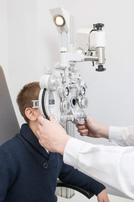 Óptico probando los ojos de un niño con dispositivos de optometría - foto de stock