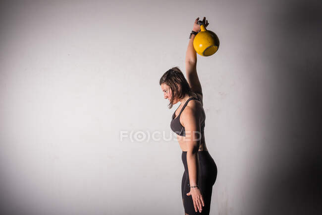 Atlético jovem concentrada mulher no sportswear acima kettlebell no ginásio — Fotografia de Stock