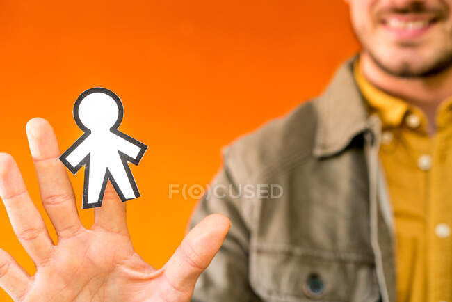 Happy guy showing paper silhouette for April fools day on orange blurred background - foto de stock