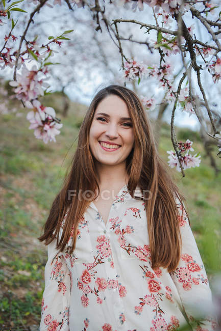 Ramoscelli di albero da frutto in fiore e attraente signora allegra guardando la fotocamera in giardino — Foto stock