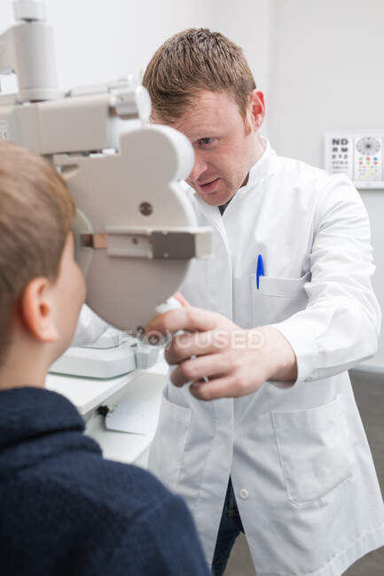 Opticida testando os olhos de um menino com dispositivos de optometria — Fotografia de Stock