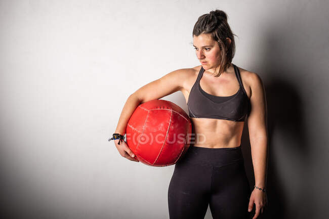 Athletische junge konzentrierte Dame in Sportbekleidung in Kreide, die im Fitnessstudio schweren Medizinball auf die Schulter klopft — Stockfoto