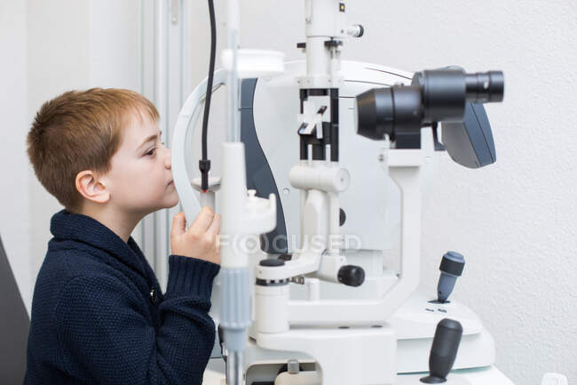 Оптиміст тестує очі хлопчика за допомогою пристроїв оптометрії — стокове фото