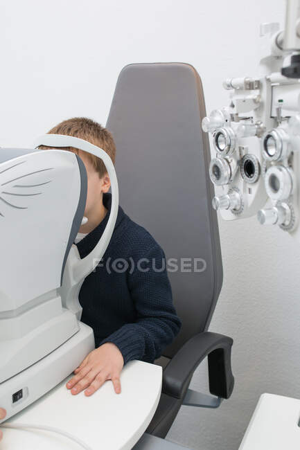 Óptico probando los ojos de un niño con dispositivos de optometría - foto de stock