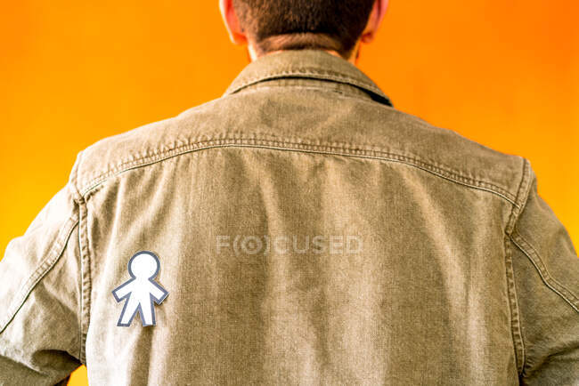 Vista trasera de chico con silueta de papel para el día de los tontos de abril en chaqueta de jean sobre fondo naranja - foto de stock