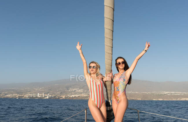 Гарні молоді жінки в окулярах і капелюхах капітана на бічній палубі дорогого човна плавають у воді в сонячний день — стокове фото