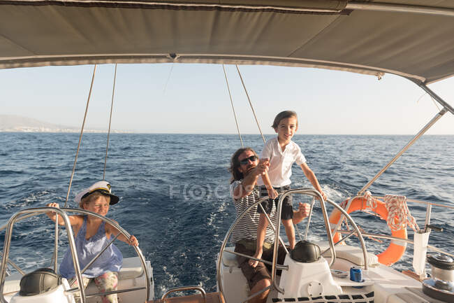 Щасливий батько з дітьми плаває на дорогому човні на морі і блакитному небі в сонячний день — стокове фото