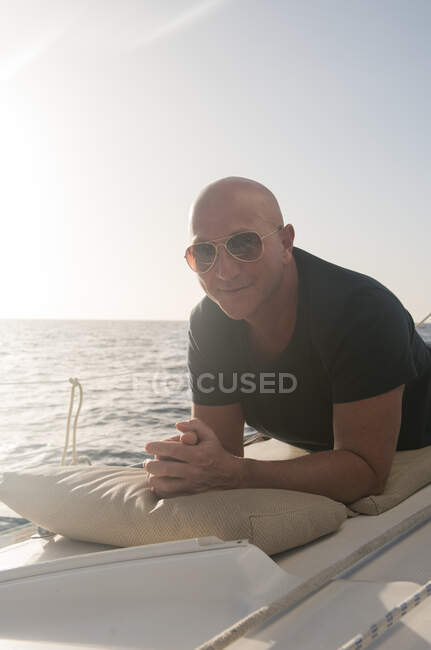 Positive male in sunglasses lying on side deck of expensive boat floating on water in sunny day — Stock Photo