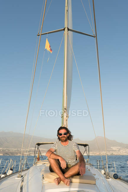 Positive bearded adult male in sunglasses sitting floating on expensive boat on sea in sunny day — Stock Photo