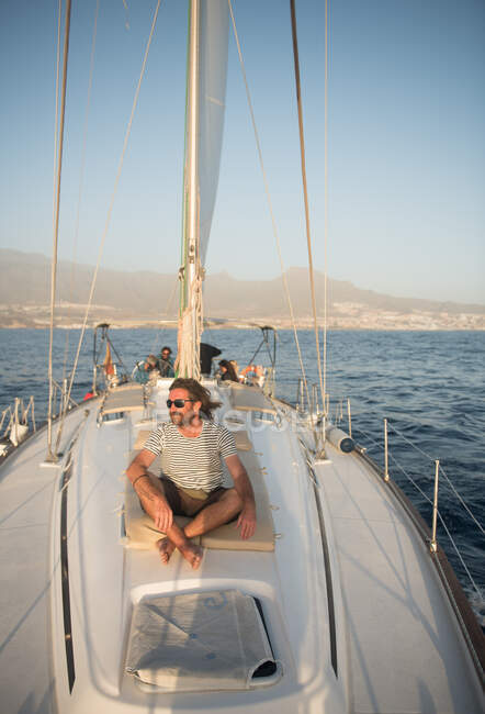 Positivo maschio adulto barbuto in occhiali da sole seduto galleggiante su costosa barca in mare nella giornata di sole — Foto stock