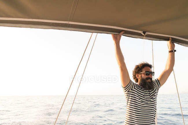 Positive bearded adult male in sunglasses floating on expensive boat on sea in sunny day — Stock Photo