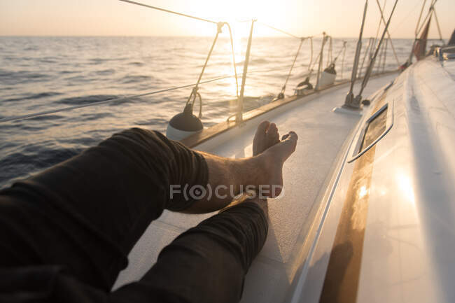 Crop legs of male lying on side deck of expensive boat floating on waving sea in sunny day — Stock Photo