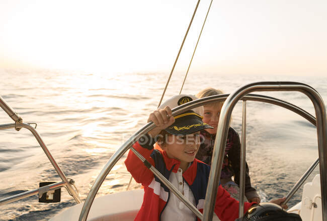 Niños positivos en sombrero de capitán flotando en barco caro en el mar en el día soleado - foto de stock