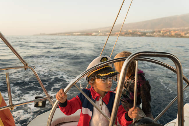 Crianças positivas em chapéu de capitão flutuando no barco caro no mar em dia ensolarado — Fotografia de Stock