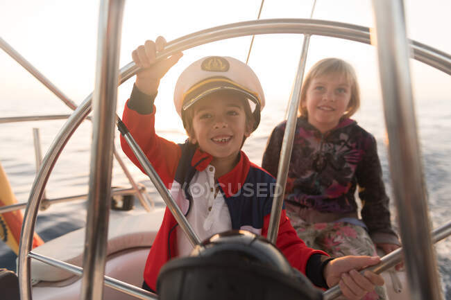 Позитивные дети в капитанской шляпе, плавающие на дорогой лодке по морю в солнечный день — стоковое фото