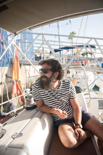 Positive bearded adult male in sunglasses resting on expensive boat in port in sunny day — Stock Photo