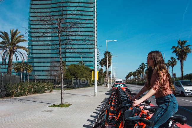 Chica tomando bicicleta de alquiler en la ciudad - foto de stock