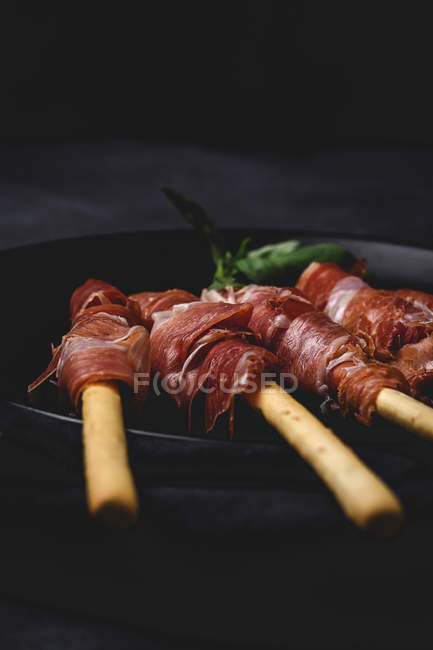 Gressinis com presunto serrano típico espanhol sobre fundo escuro — Fotografia de Stock