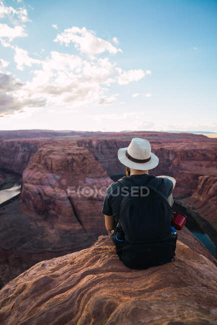Вид сзади бородатого парня с рюкзаком, смотрящего на красивый каньон и спокойную реку в солнечный день на западном побережье США — стоковое фото