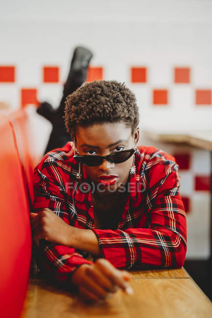 Confiante mulher afro-americana deitada em assentos no café e olhando para a câmera — Fotografia de Stock