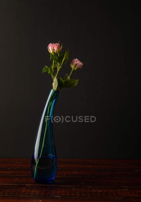Fleurs roses dans un vase en verre élégant sur plateau en bois sur fond sombre — Photo de stock