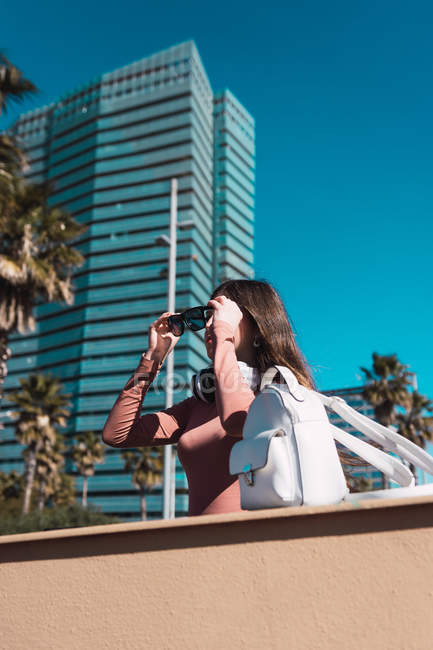Chica poniéndose gafas de sol en la ciudad con palmeras - foto de stock