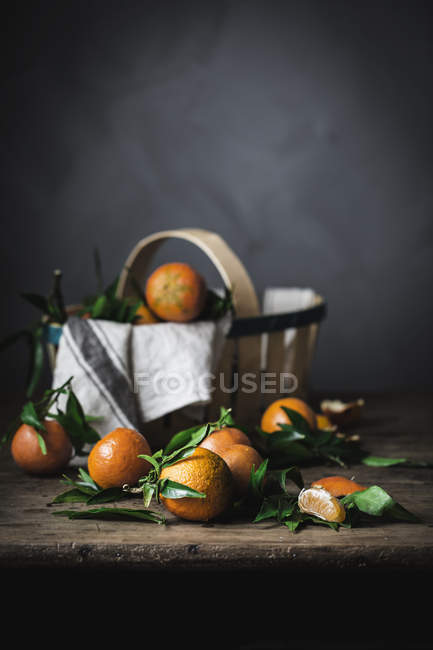 Mandarini maturi con foglie e cesto su tavolo di legno grezzo — Foto stock
