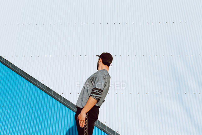 Парень в стильном наряде выполняя флип возле стены современного здания на городской улице — стоковое фото
