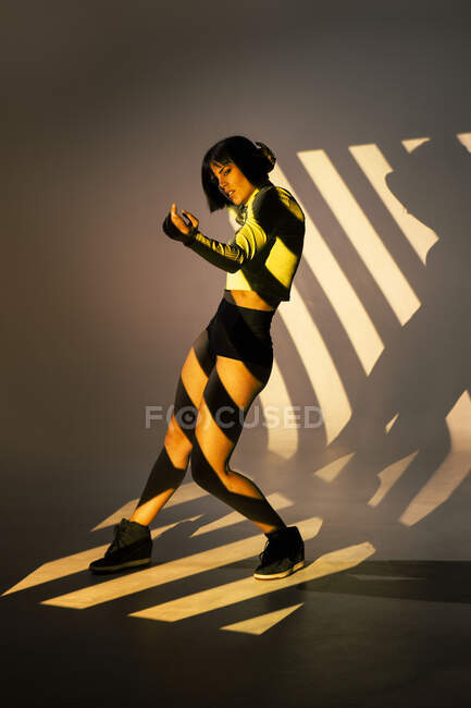 Attraente sottile femminile che esegue movimento di danza sotto la luce intensa dalla finestra — Foto stock