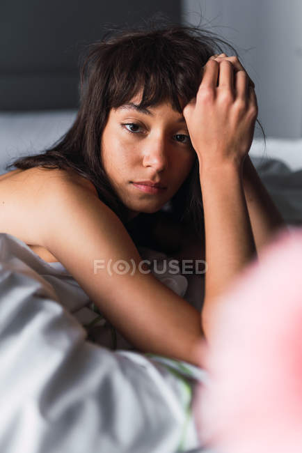 Junge attraktive Frau blickt in die Kamera, während sie sich im Schlafzimmer auf dem Bett ausruht — Stockfoto