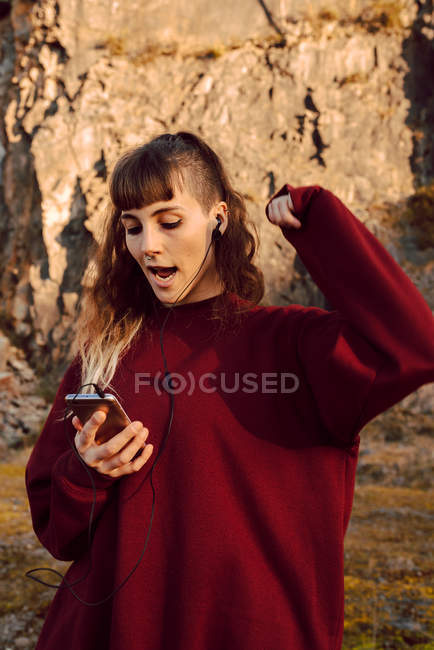Молода хіпстерка з посиленою рукою слухає музику на мобільному телефоні і танцює в сільській місцевості — стокове фото