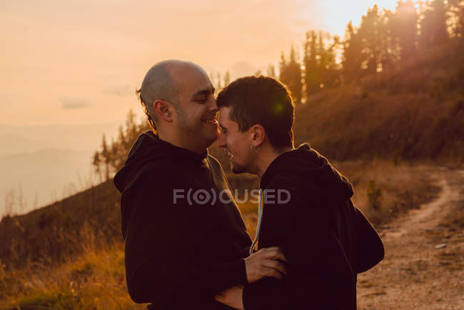 Rindo casal homossexual abraçando no caminho nas montanhas em dia ensolarado — Fotografia de Stock