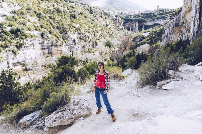 Уверенная женщина в повседневной одежде, стоящая на каменистой земле против удивительных гор в солнечный день в сельской местности — стоковое фото