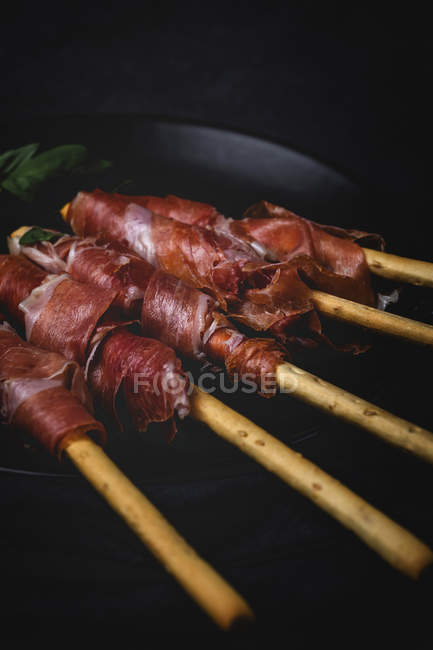 Gressinis with spanish typical serrano ham on plate on dark background — Stock Photo