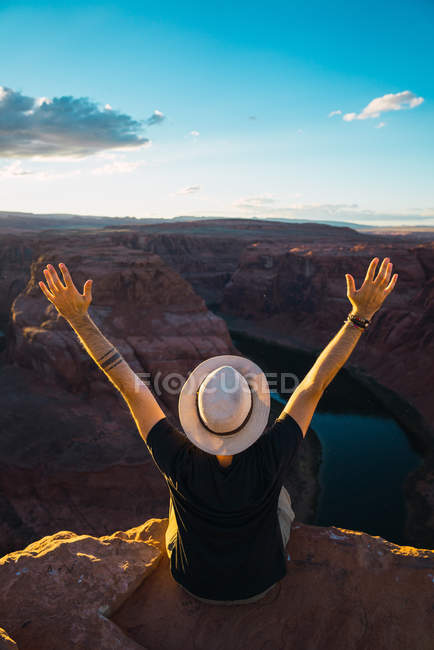 Обратный вид человека, протягивающего оружие и любующегося видом каньона на небо во время путешествия по западному побережью США — стоковое фото