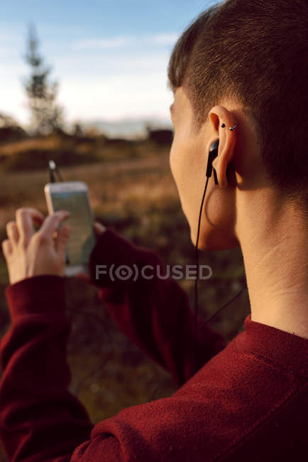 Jovem hipster mulher com piercing e fones de ouvido ouvir música com telefone celular no campo — Fotografia de Stock