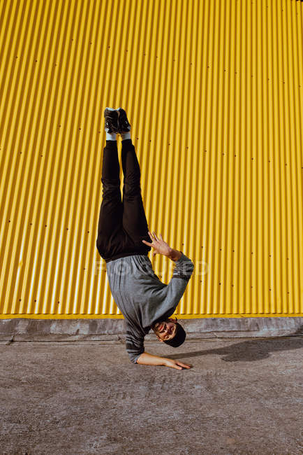 Young guy performing handstand while dancing near wall of modern building on city street — Stock Photo