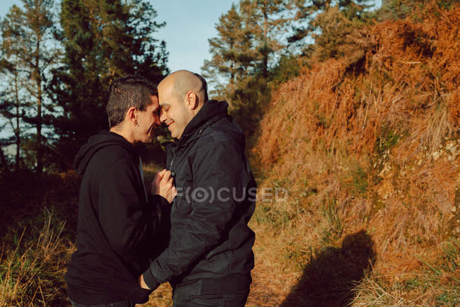 Happy homosexual couple hugging on path in forest in sunny day — Stock Photo