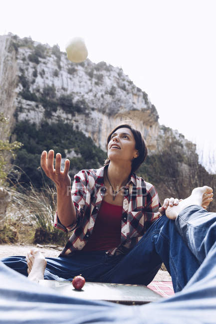 Чоловік лежить на племені з жінкою, сидячи поруч і кидаючи яблуко, насолоджуючись разом на пікніку в природі — стокове фото