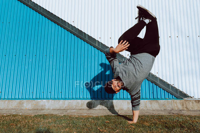 Young guy performing handstand and looking at camera while dancing near wall of modern building on city street — Stock Photo