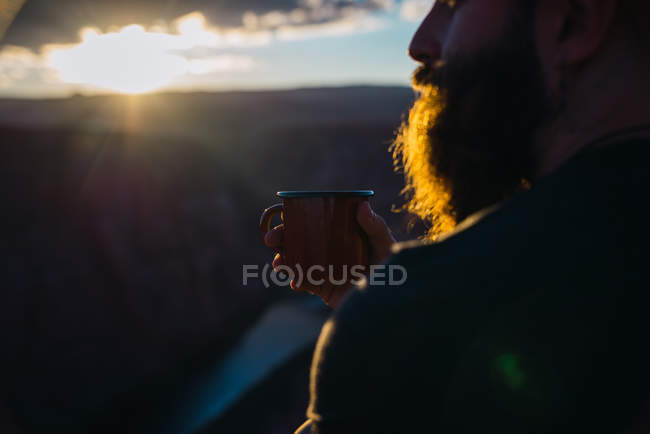 Seitenansicht des bärtigen Typen, der die untergehende Sonne betrachtet, während er in der Nähe eines wunderschönen Canyons an der Westküste der USA sitzt — Stockfoto