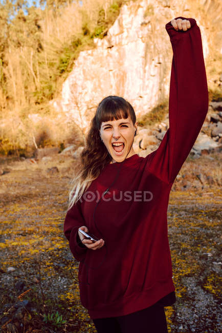 Молодая хипстерша с поднятой рукой слушает музыку с мобильного телефона и танцует в сельской местности — стоковое фото