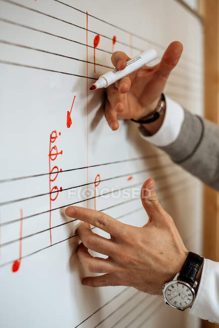 Hombre irreconocible manos escribiendo notas musicales en una pizarra blanca en una escuela de conservatorio - foto de stock