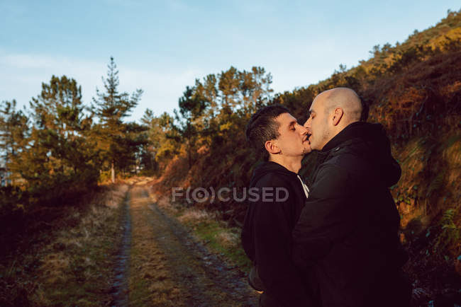 Glückliches homosexuelles Paar umarmt und küsst sich bei sonnigem Wetter auf der Strecke im Wald — Stockfoto