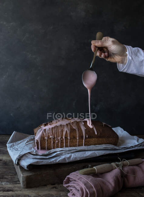 Рука человека с ложкой льется сверху на свежий апельсиновый торт, размещенный на салфетке возле полотенца и кисти на черном фоне — стоковое фото