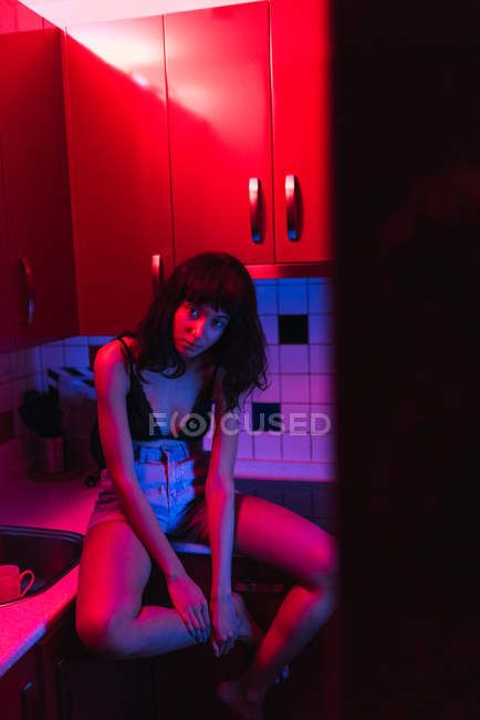 Sinnliche junge brünette Frau in Dessous schaut in die Kamera und sitzt in der Küche zwischen Rötungen — Stockfoto