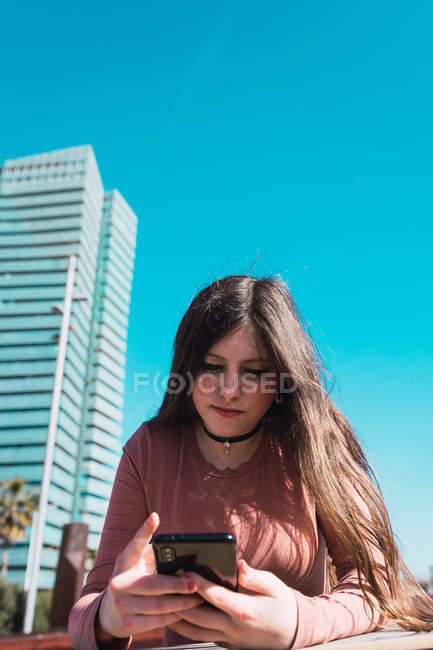 Підліток дивиться на свій смартфон на вулиці в сонячний день. — стокове фото