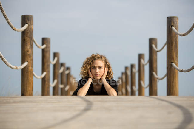 Jeune femme couchée sur le devant sur une passerelle en bois dans la nature et regardant la caméra — Photo de stock