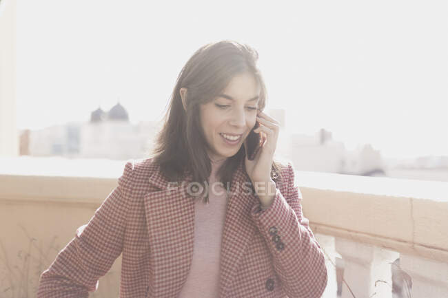 Jeune dame élégante avec la main sur la hanche parler sur le téléphone mobile sur le balcon dans la journée ensoleillée — Photo de stock