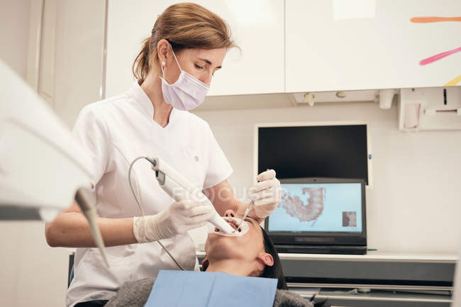 Mulher em luvas e máscara usando equipamentos modernos para varredura de dentes de paciente do sexo feminino em consultório odontológico — Fotografia de Stock